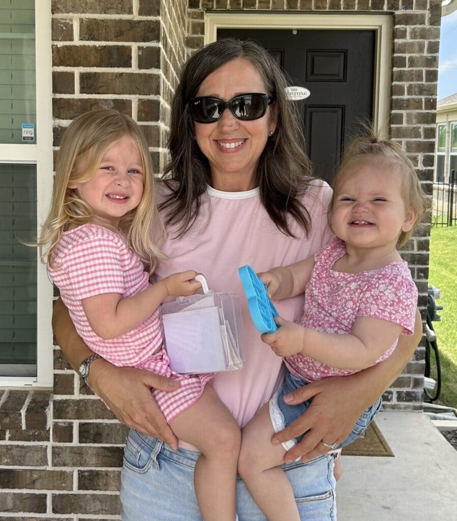 A woman holding two children outside of a house.