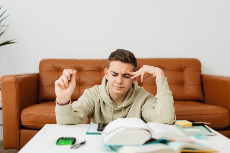 Teenage boy studying and experiencing academic struggles on a brown sofa.