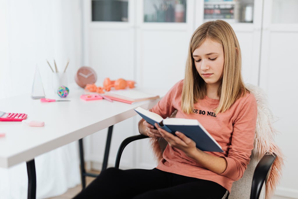 A teenage girl sits comfortably in a chair reading a book in a stylish home office.